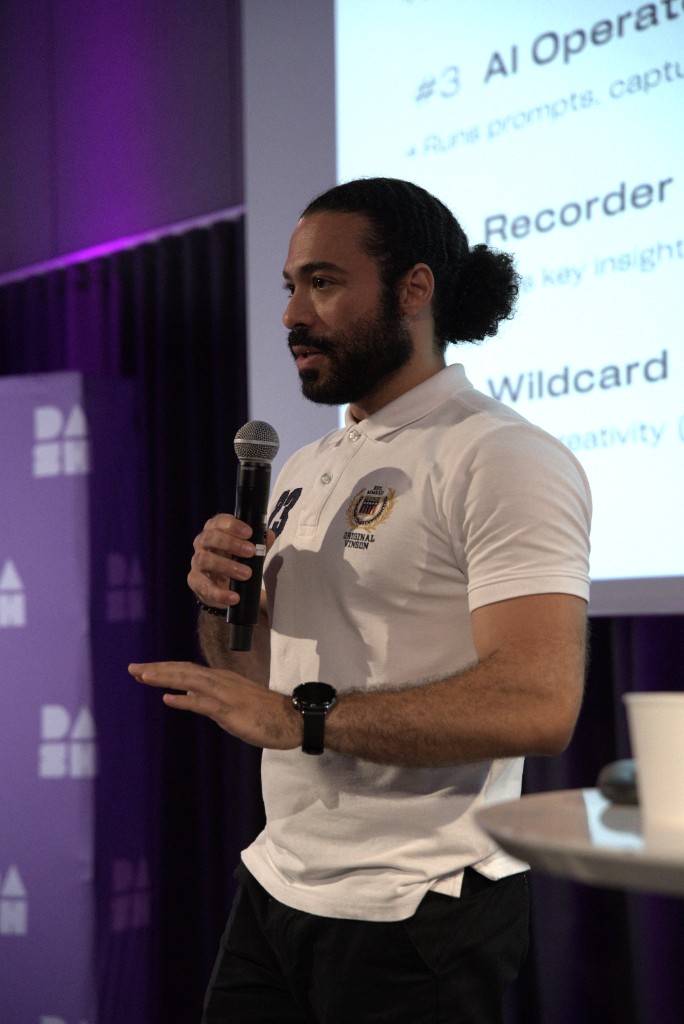 Aly Metwaly speaking on stage at DASH with purple stage lighting and a handheld microphone